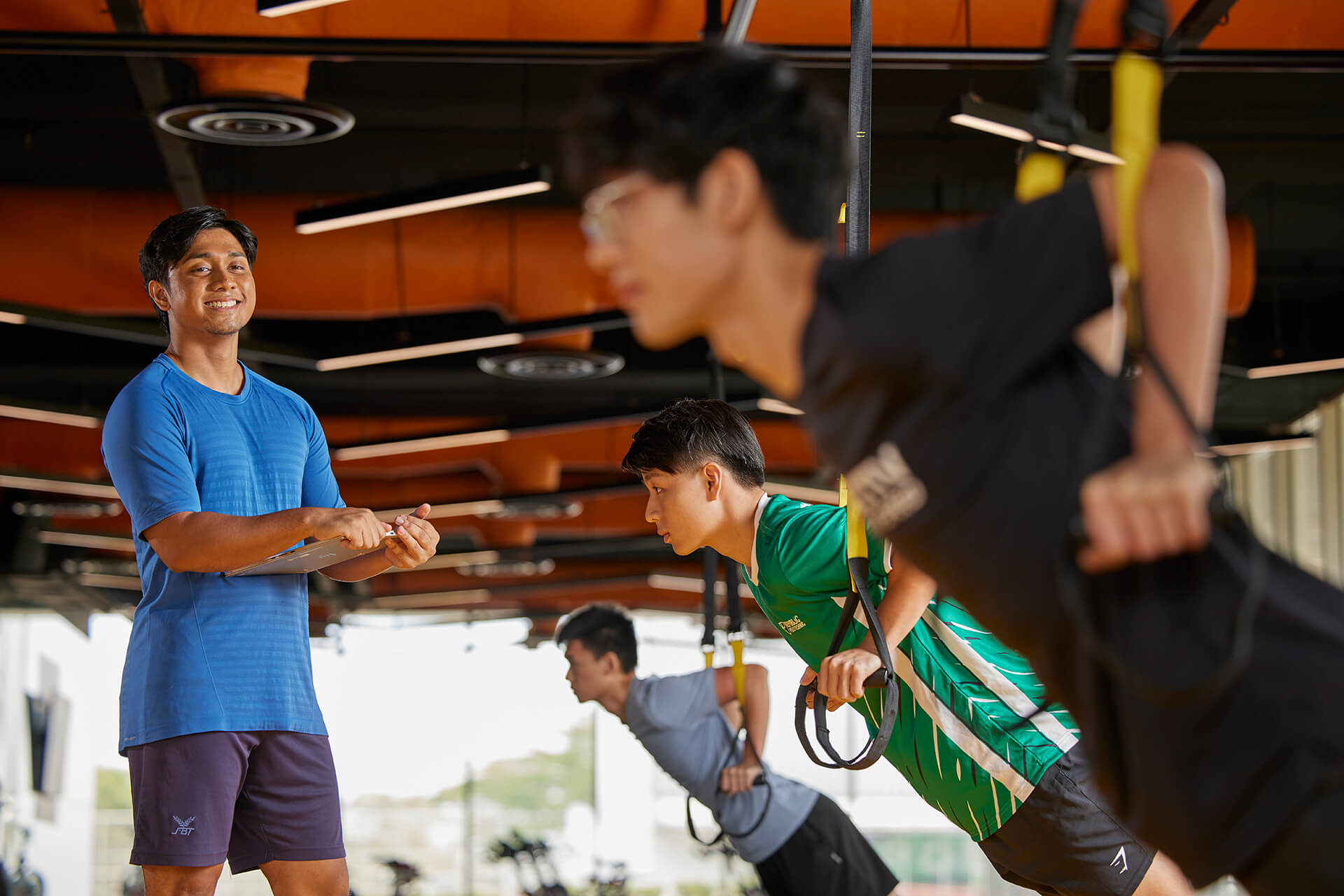 A fitness coach smiles on as he coaches his students exercising in a fitness class