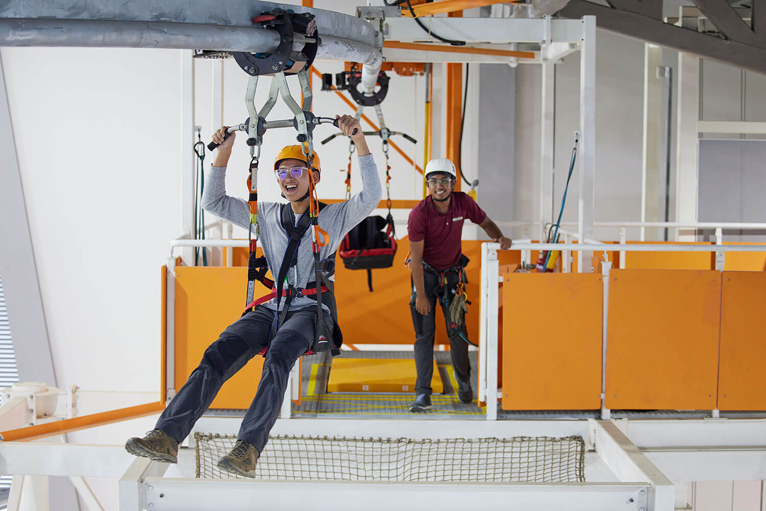 An outdoor education student in safety helmet and harness gliding down the rollglider while his facilitator watches on