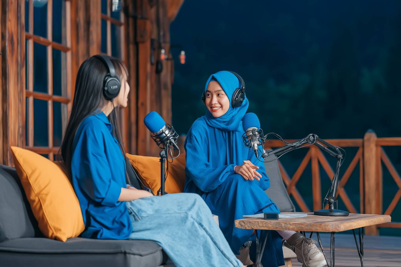 Two women recording podcast with professional microphones and headphones in cozy outdoor setting