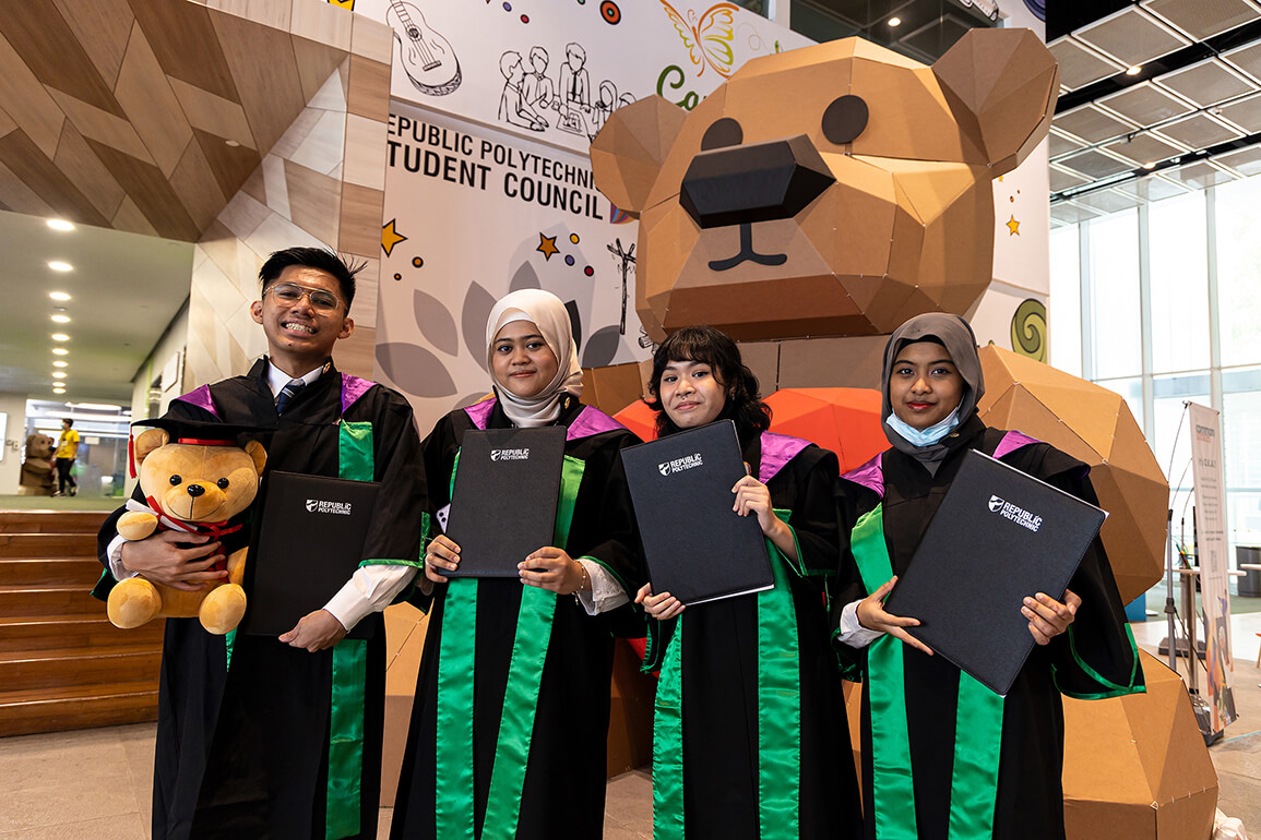 Graduates posing with their diplomas in front of the RP Bear