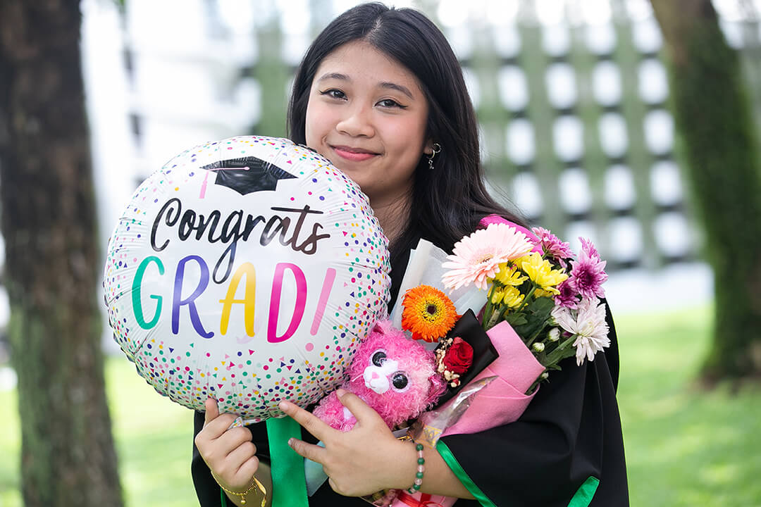 Graduate smiling and pointing at a graduation balloon