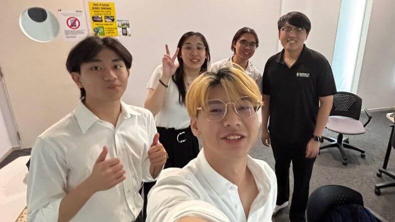 Group of students taking a selfie together in a classroom setting during a project session.