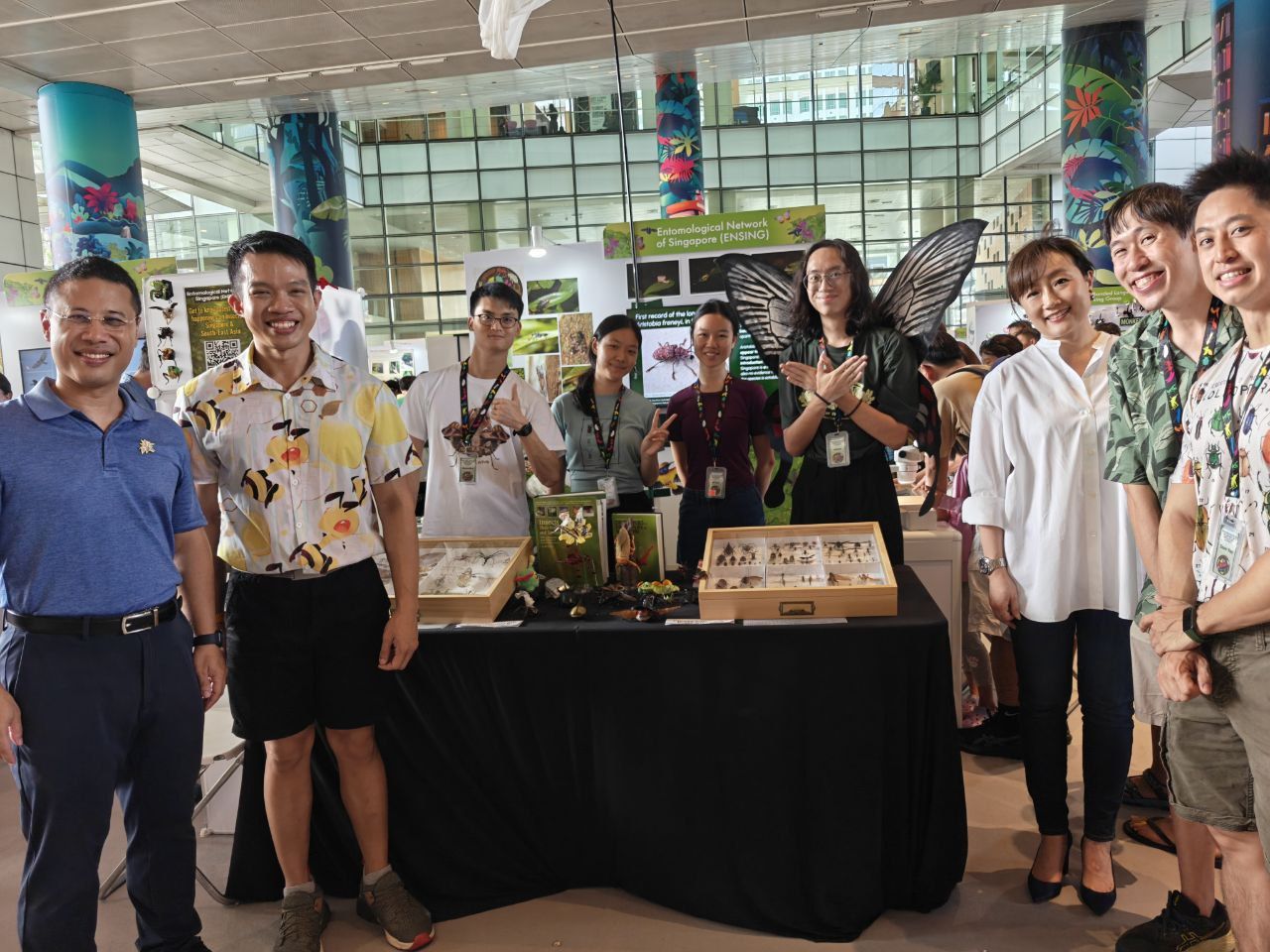 Group photo of staff and students at an entomology outreach booth, showcasing insect specimens and educational displays at a public exhibition.